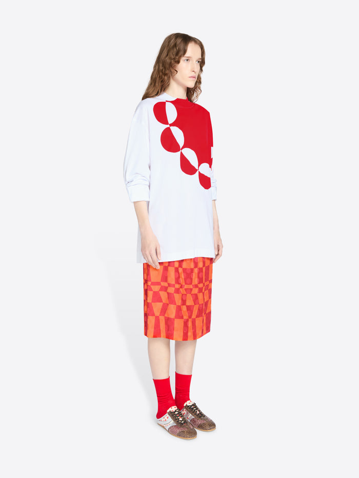 Person wearing a white shirt with red geometric design and a red patterned skirt on a white background - Dries Van Noten