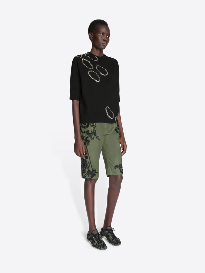 Model wearing a black top with circular designs and green shorts on a white background - Dries Van Noten