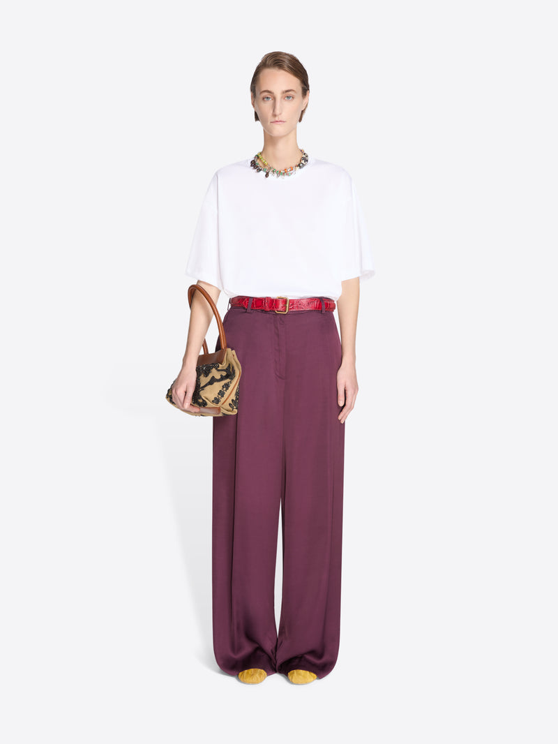 Model wearing a white top and burgundy pants with a small handbag on a light gray background - Dries Van Noten