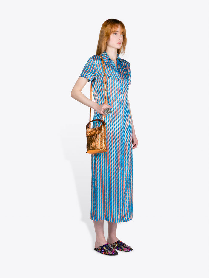 Woman wearing a blue patterned dress holding a brown handbag on a white background