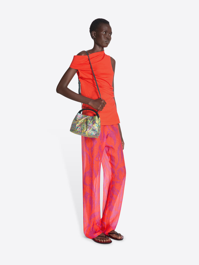 Model wearing a bright orange top and colorful pants, holding a floral handbag on a white background - Dries Van Noten