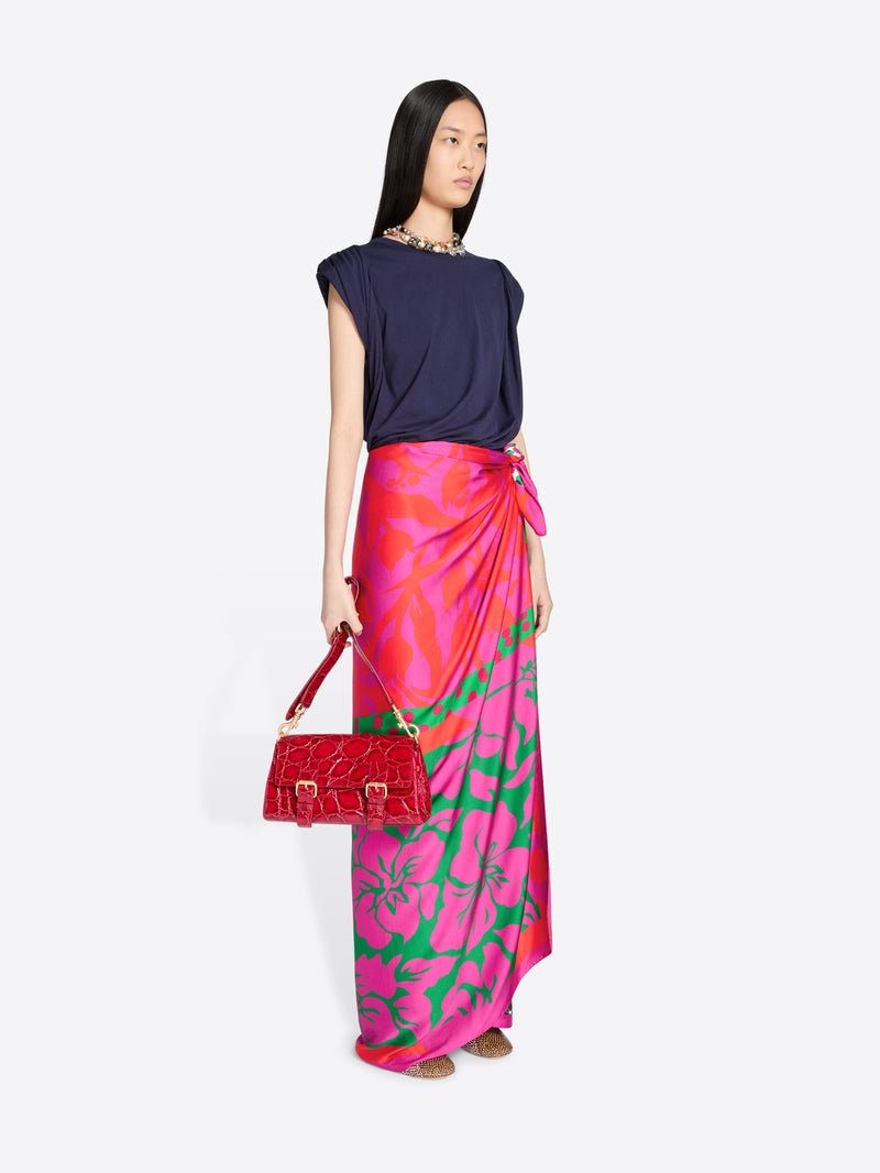 Woman wearing a colorful floral skirt and holding a red handbag on a white background - Dries Van Noten