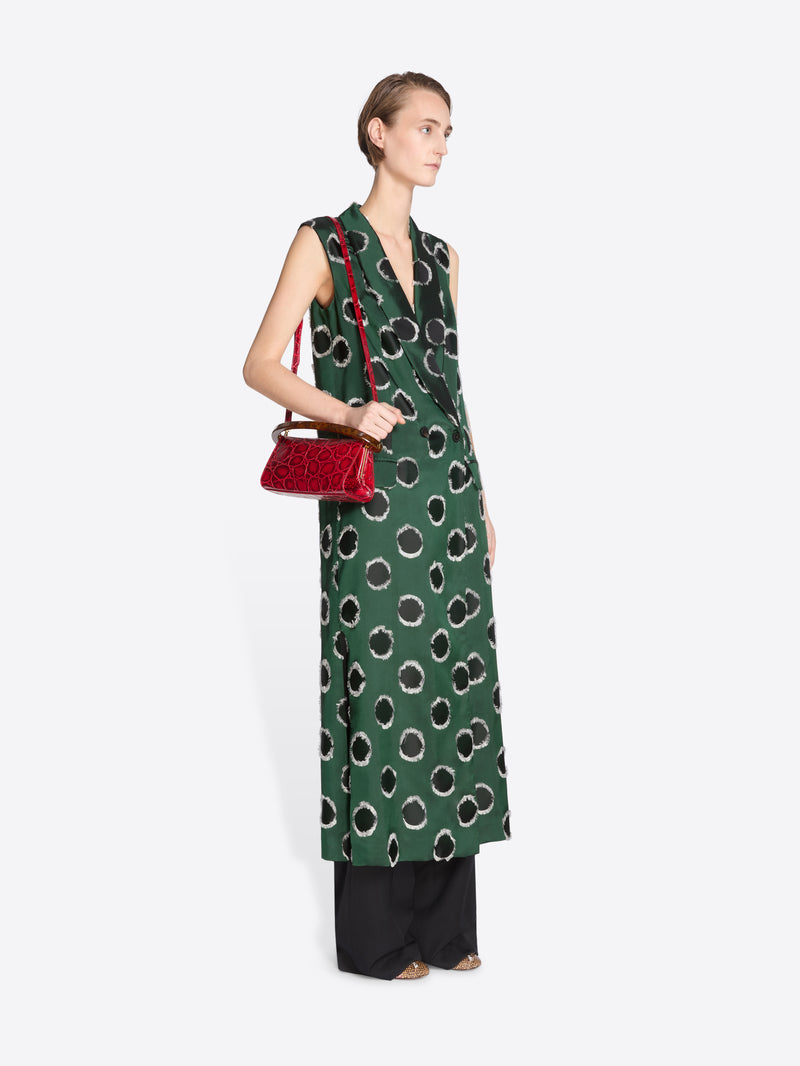 Woman wearing a green patterned dress holding a red handbag on a white background - Dries Van Noten