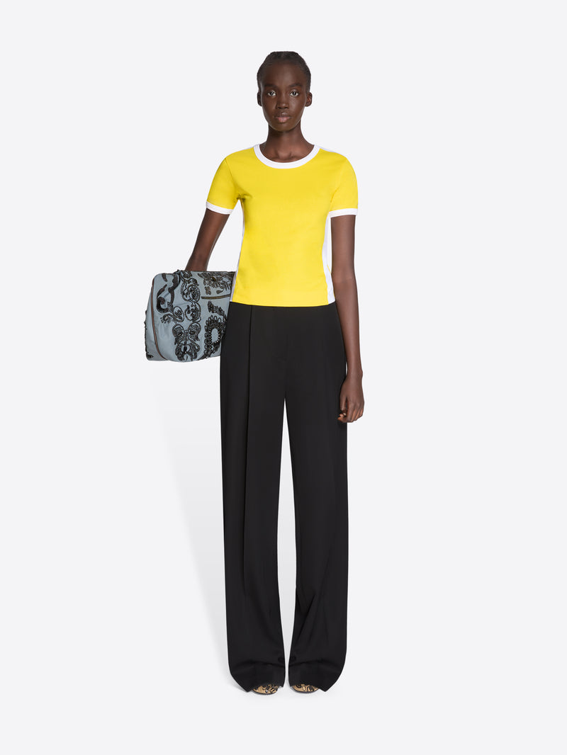 Woman wearing a yellow top and black pants holding a patterned handbag on a white background - Dries Van Noten