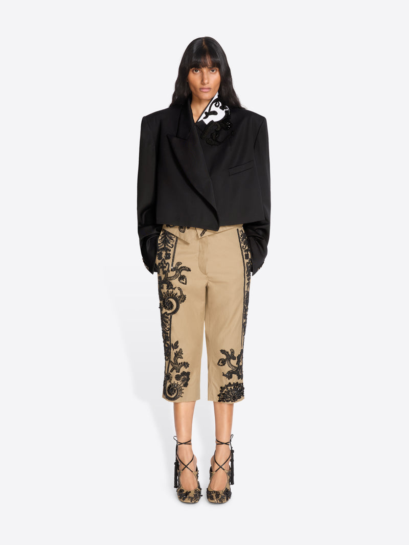 Woman wearing a black blazer and beige pants with black lace details on a white background - Dries Van Noten