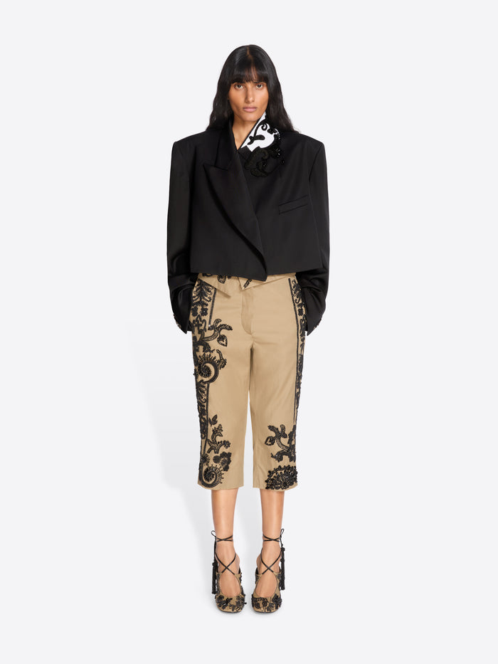 Woman wearing a black blazer and beige pants with black lace details on a white background - Dries Van Noten