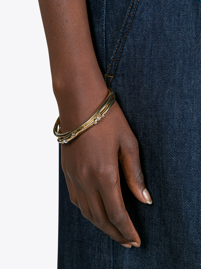 Gold bracelet on a wrist with a dark denim background - Dries Van Noten