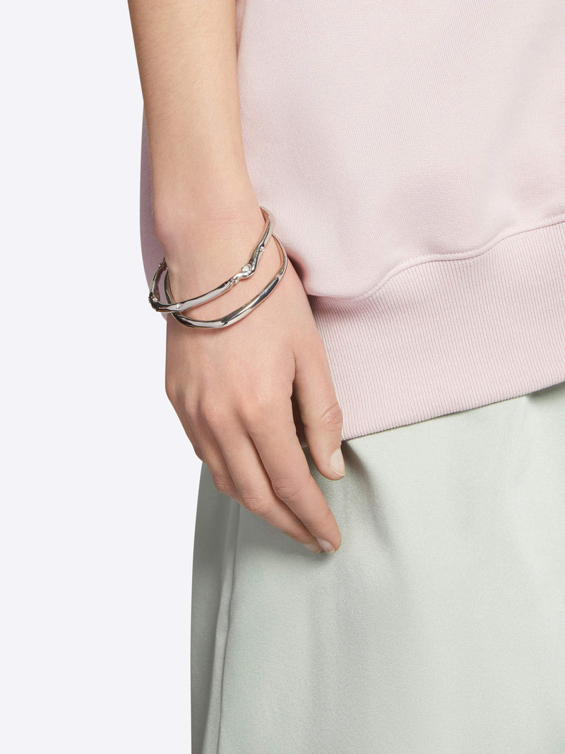 Hand wearing multiple silver bracelets on a plain background - Dries Van Noten