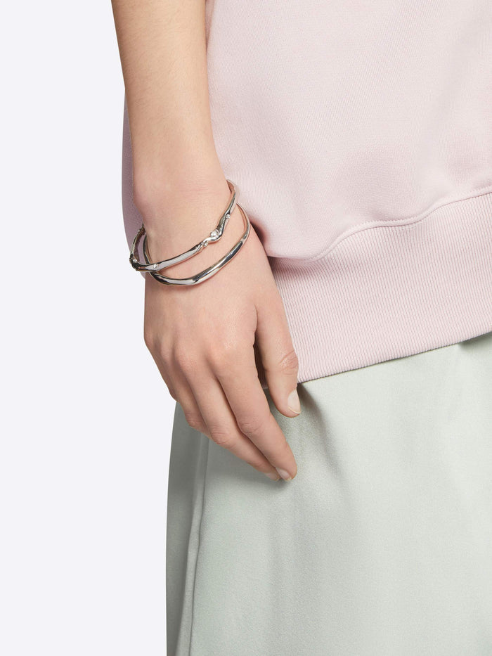 Hand wearing multiple silver bracelets on a plain background - Dries Van Noten