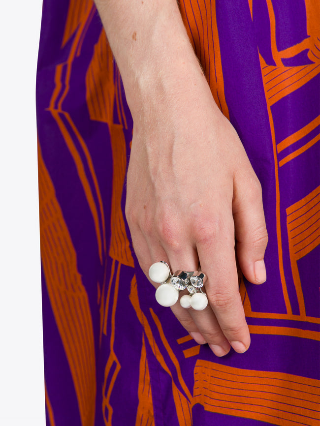 Hand wearing multiple rings with a purple and orange patterned fabric background
