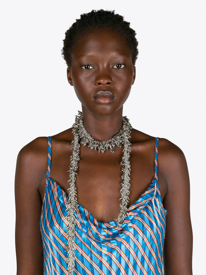 Woman wearing a blue striped dress with thin straps and a long necklace on a white background