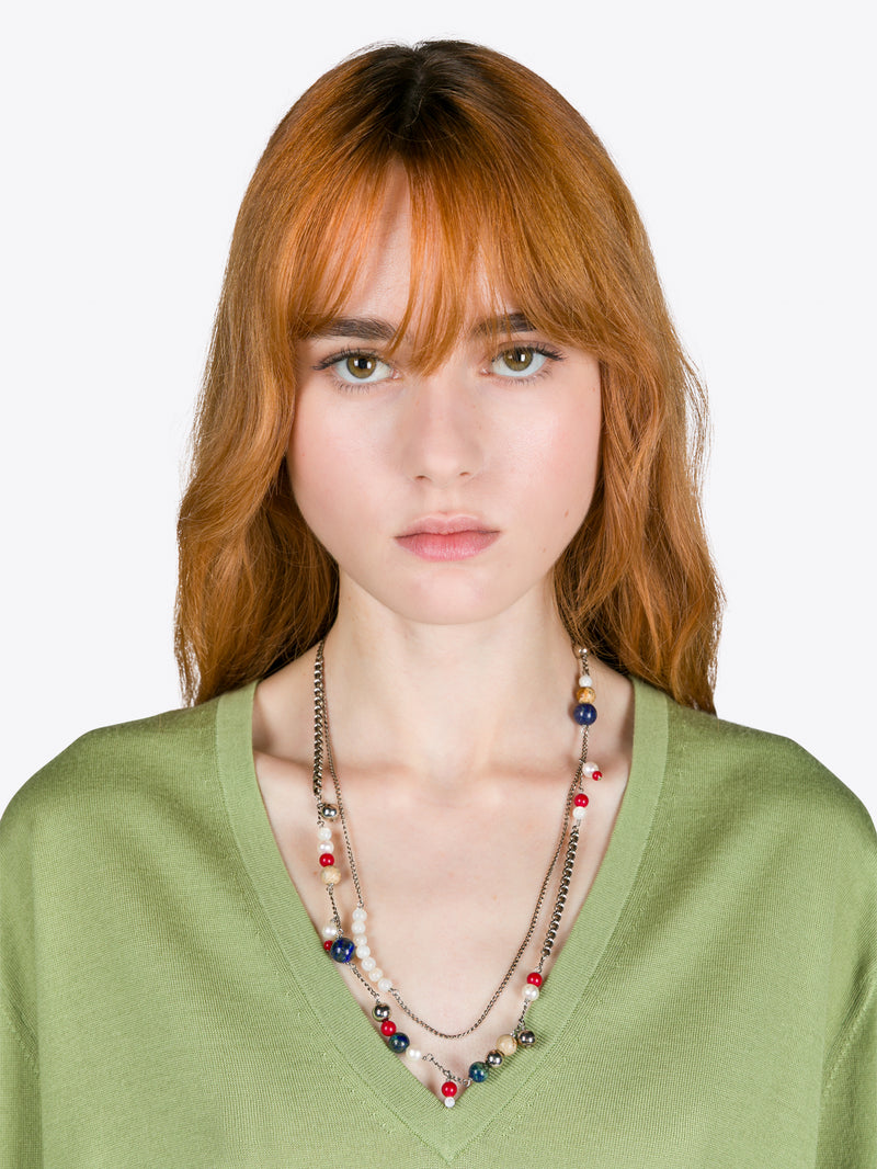 Woman wearing a green top and colorful necklace against a white background