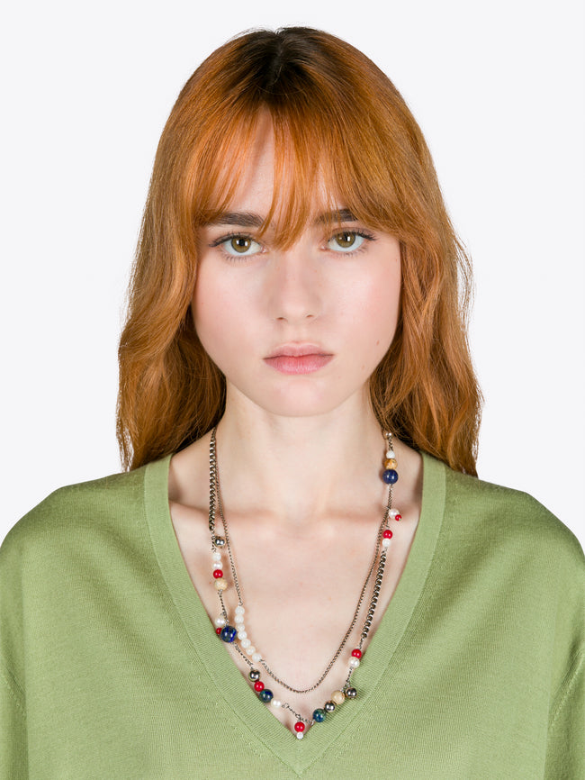 Woman wearing a green top and colorful necklace against a white background
