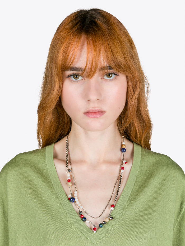 Woman wearing a green top and colorful necklace against a white background