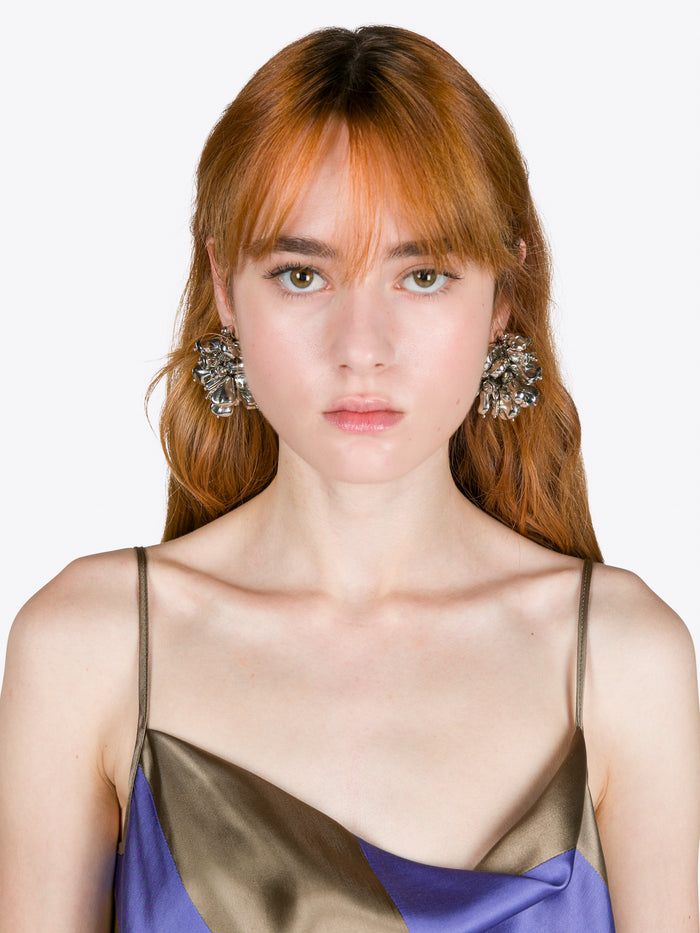 Woman wearing a sheer top with floral earrings on a white background