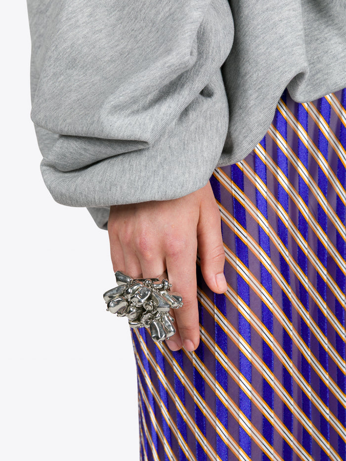Person wearing a gray sweatshirt and blue plaid skirt with a decorative ring on a white background