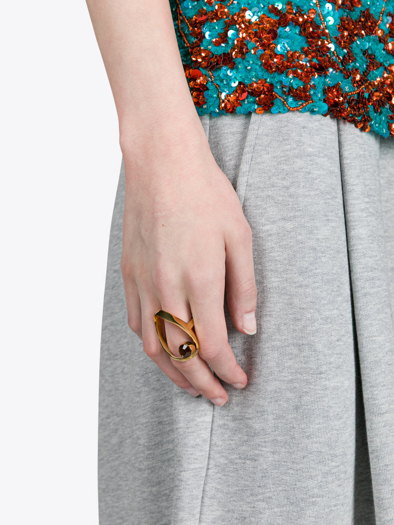 Close-up of a hand wearing a gold ring with a blue sequined top and gray pants.