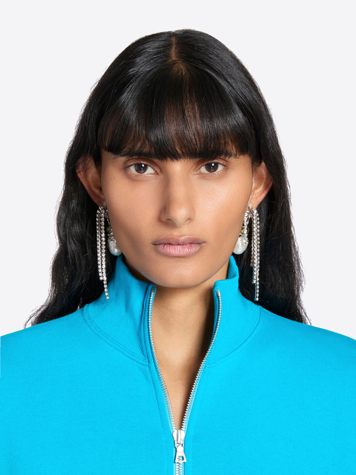 Woman wearing a blue jacket with long earrings on a white background - Dries Van Noten