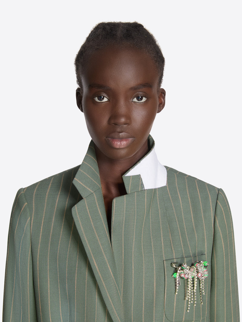 Woman wearing a green pinstripe blazer with a brooch on a white background - Dries Van Noten