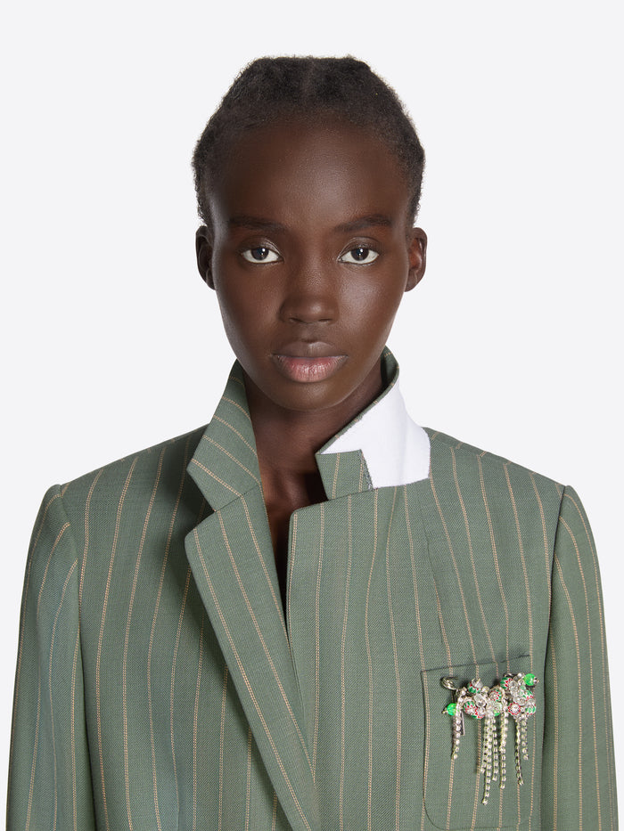 Woman wearing a green pinstripe blazer with a brooch on a white background - Dries Van Noten