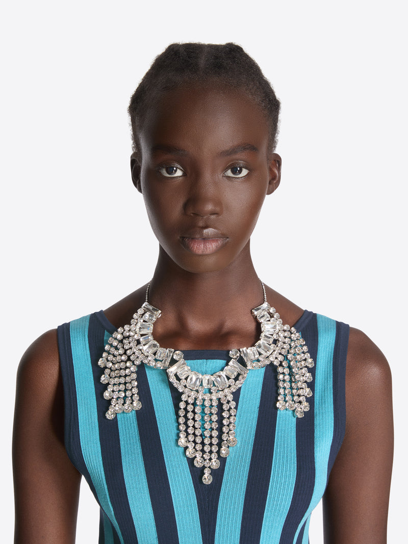 Woman wearing a blue and black striped dress with a large silver necklace on a white background - Dries Van Noten