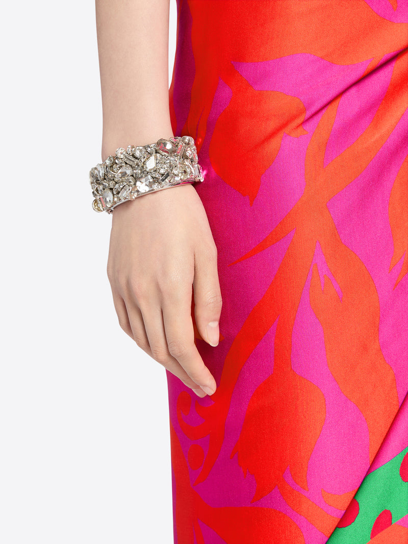 Hand wearing a silver bracelet on a red and pink floral dress. - Dries Van Noten