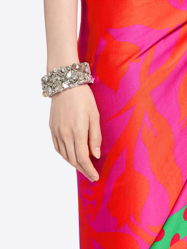 Hand wearing a silver bracelet on a red and pink floral dress. - Dries Van Noten