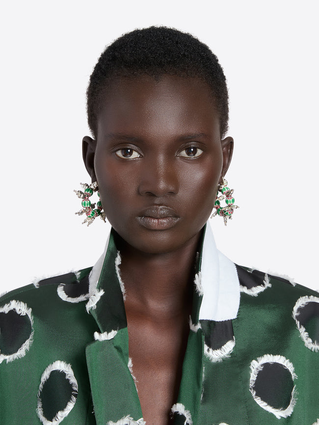 Woman wearing a green patterned outfit with large earrings on a white background - Dries Van Noten