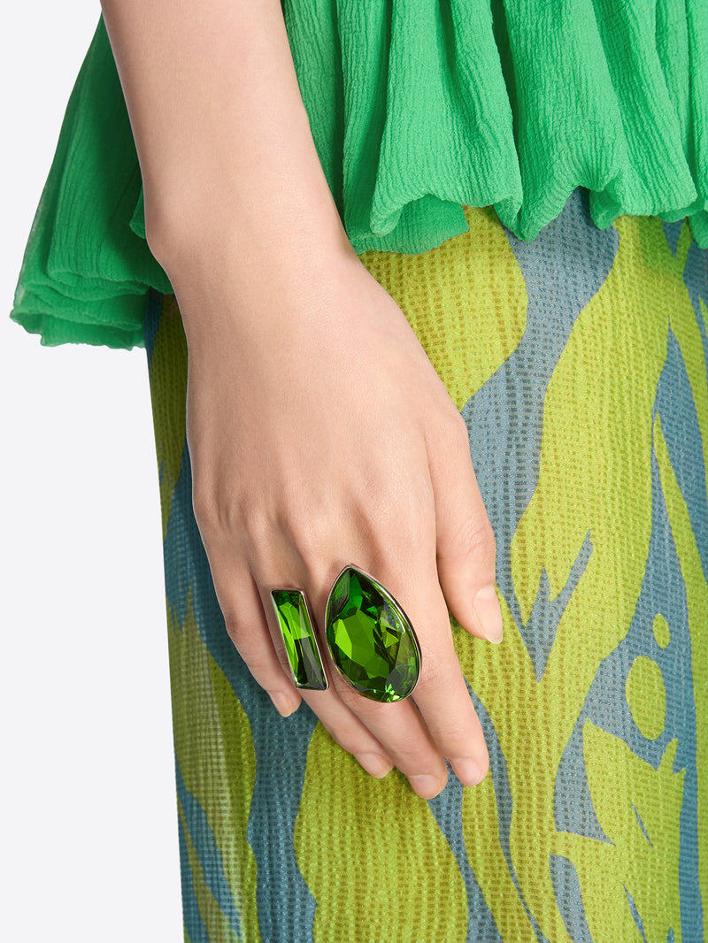 Hand wearing a green ring with a patterned fabric background - Dries Van Noten