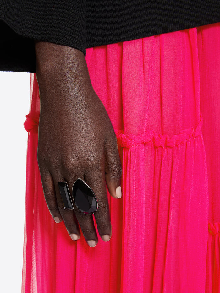 Hand wearing a black ring on a bright pink fabric background - Dries Van Noten