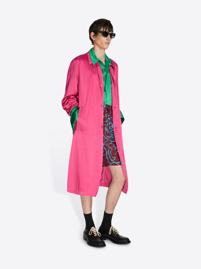 Person wearing a bright pink coat with green accents on a white background