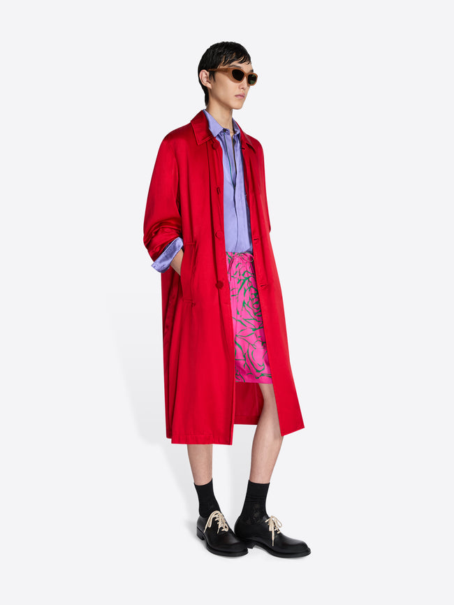 Person wearing a red coat over colorful shorts on a white background