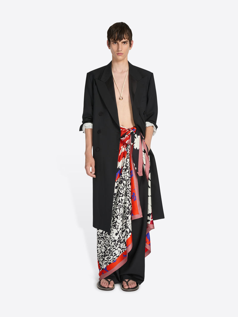 Model wearing a black outfit with a colorful scarf wrapped as a skirt on a white background - Dries Van Noten