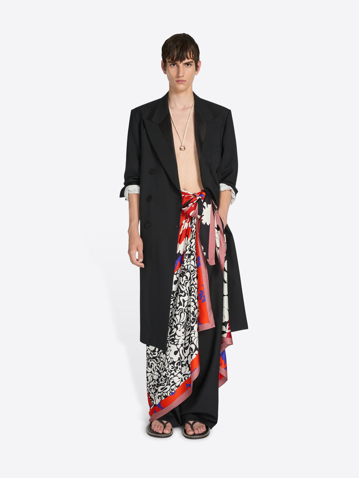Model wearing a black outfit with a colorful scarf wrapped as a skirt on a white background - Dries Van Noten