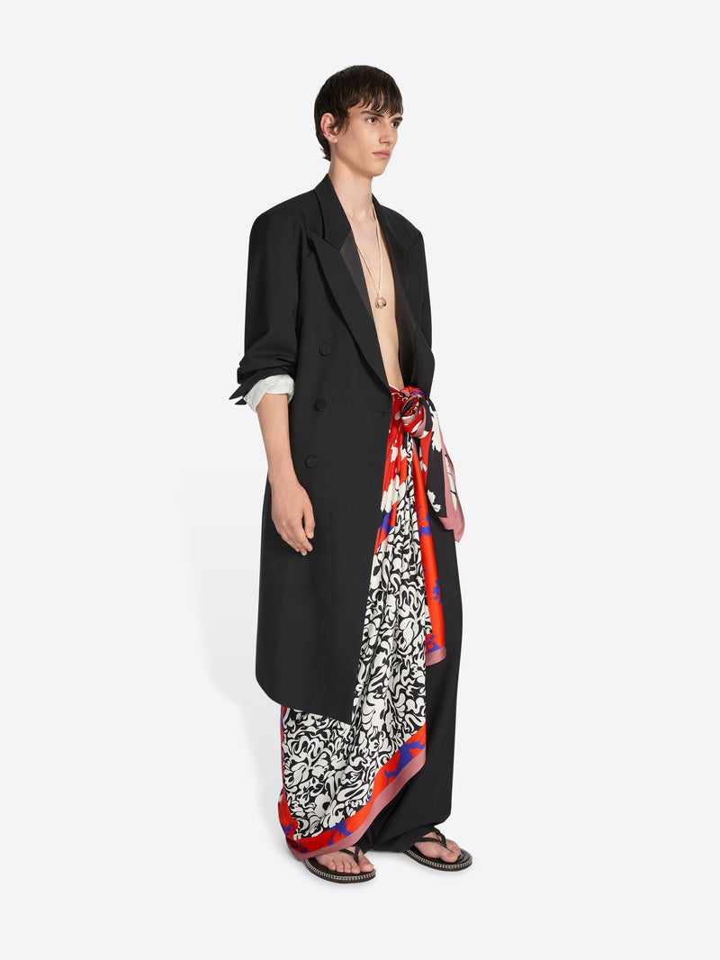 Model wearing a black outfit with a colorful scarf wrapped as a skirt on a white background - Dries Van Noten