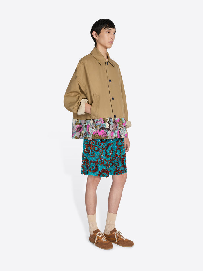 Person wearing a beige jacket, and colorful shorts on a white background - Dries Van Noten