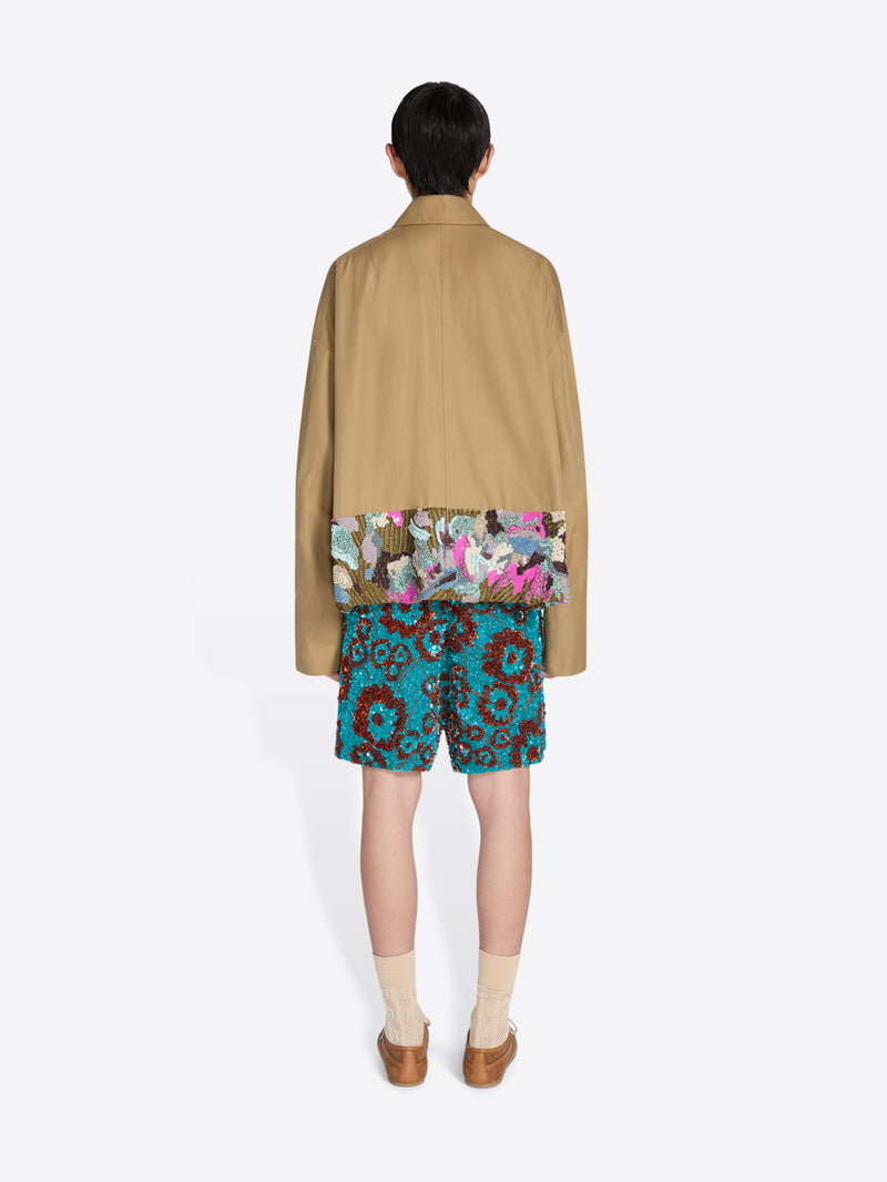 Person wearing a beige jacket and colorful floral shorts on a white background - Dries Van Noten