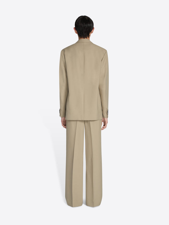 Person wearing a beige suit standing against a white background