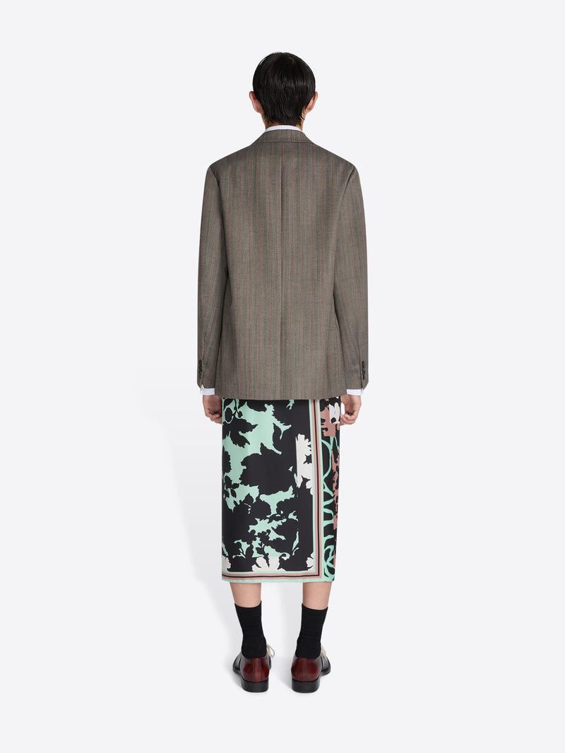 Person wearing a patterned skirt and brown jacket on a white background