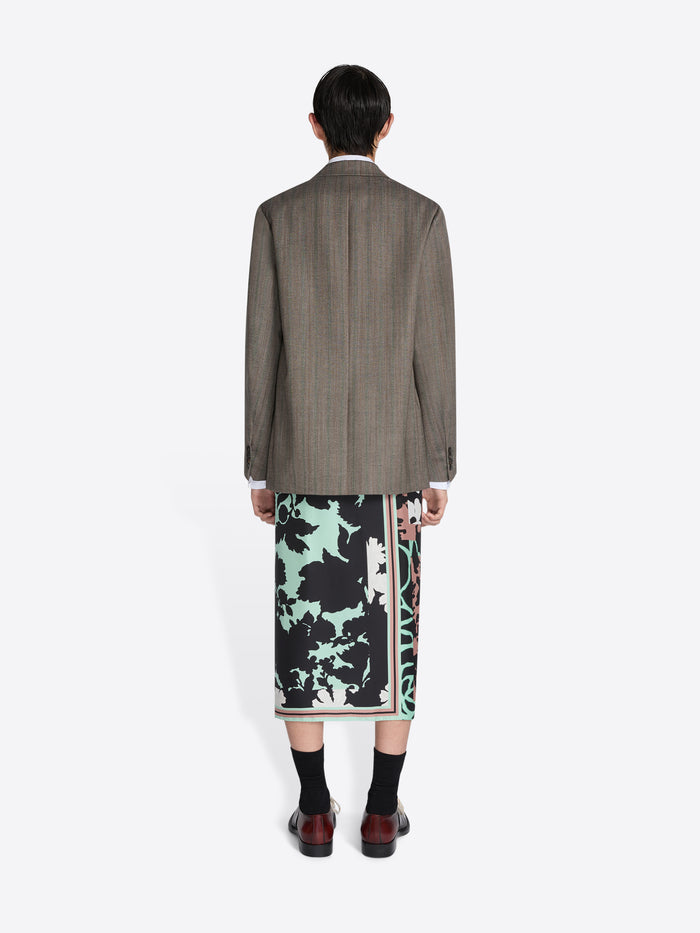 Person wearing a patterned skirt and brown jacket on a white background