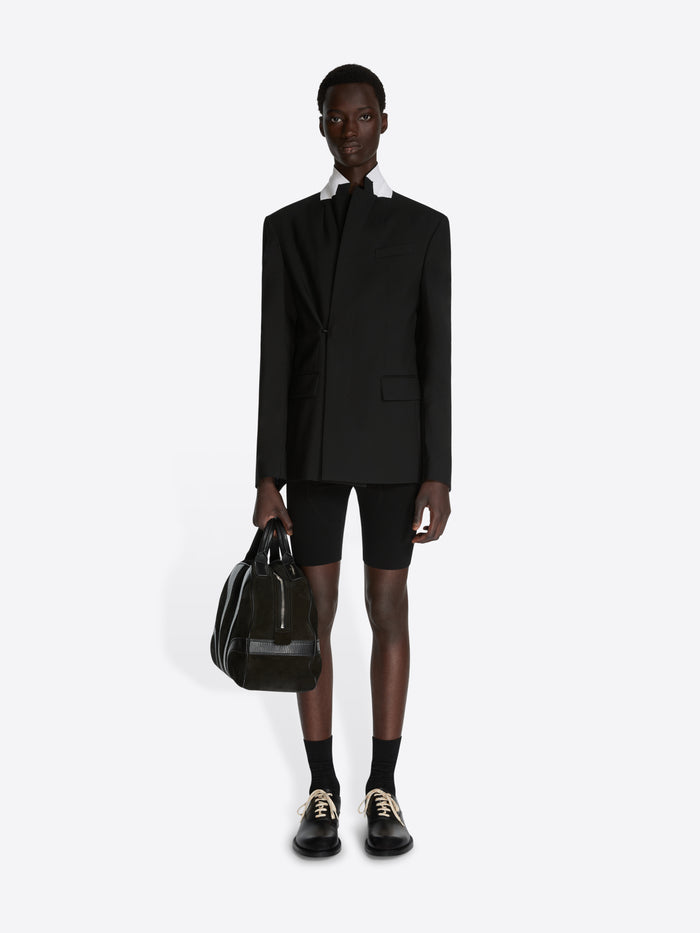 Person wearing a black suit with shorts holding a black bag on a white background - Dries Van Noten