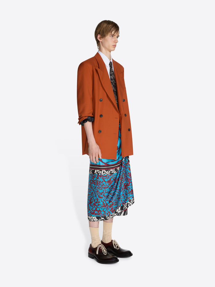 Person wearing a brown coat over a patterned dress on a white background