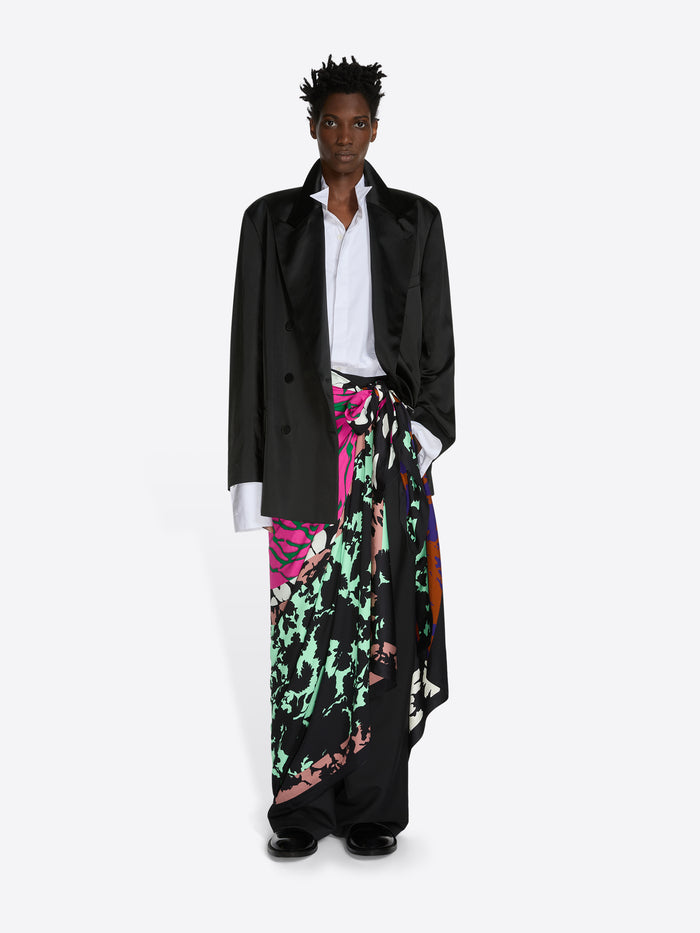 Person wearing a black coat, white shirt, and colorful floral skirt on a white background