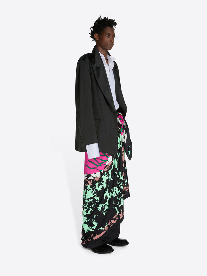 Person wearing a black coat over a colorful skirt on a white background
