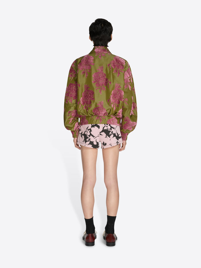 Person wearing a green floral jacket and pink floral shorts on a white background