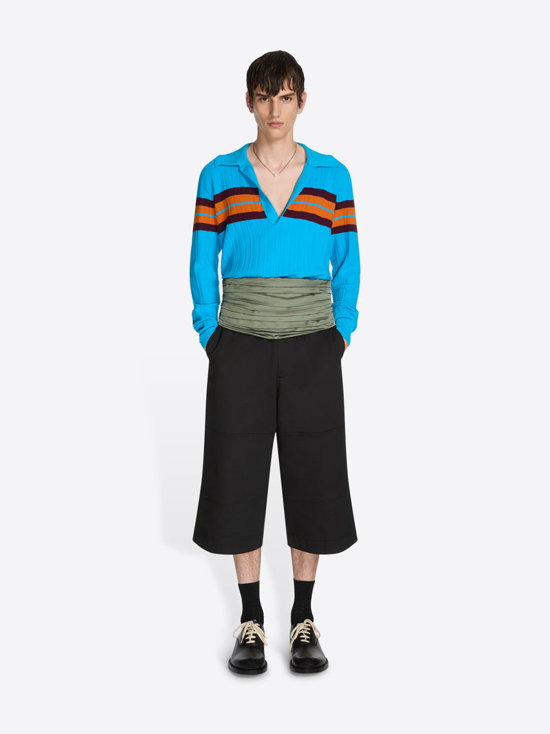 Person wearing a blue sweater with colorful stripes and black pants on a white background - Dries Van Noten