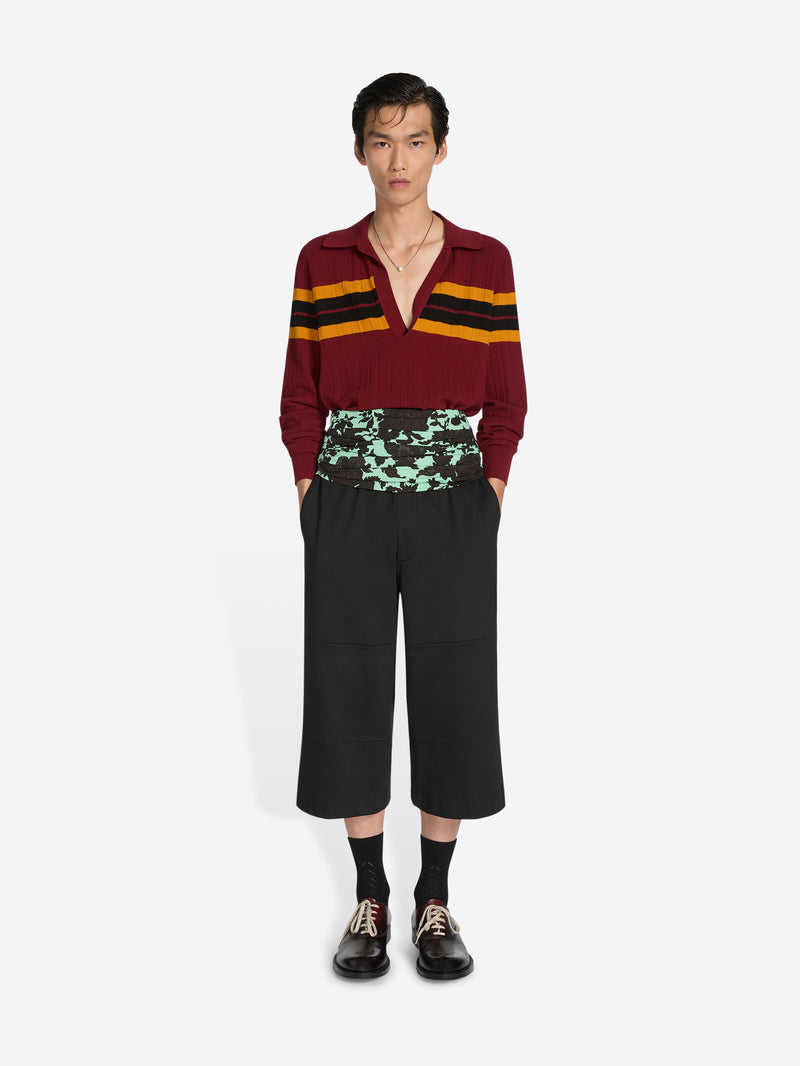 Person wearing a maroon sweater with yellow and black stripes and black pants on a white background