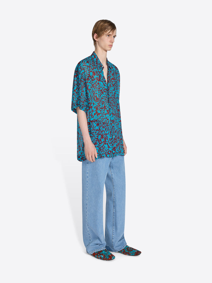 Person wearing a blue patterned shirt and jeans on a white background - Dries Van Noten