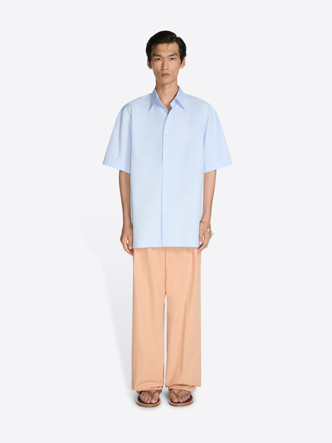 Person wearing a light blue shirt and beige pants on a white background