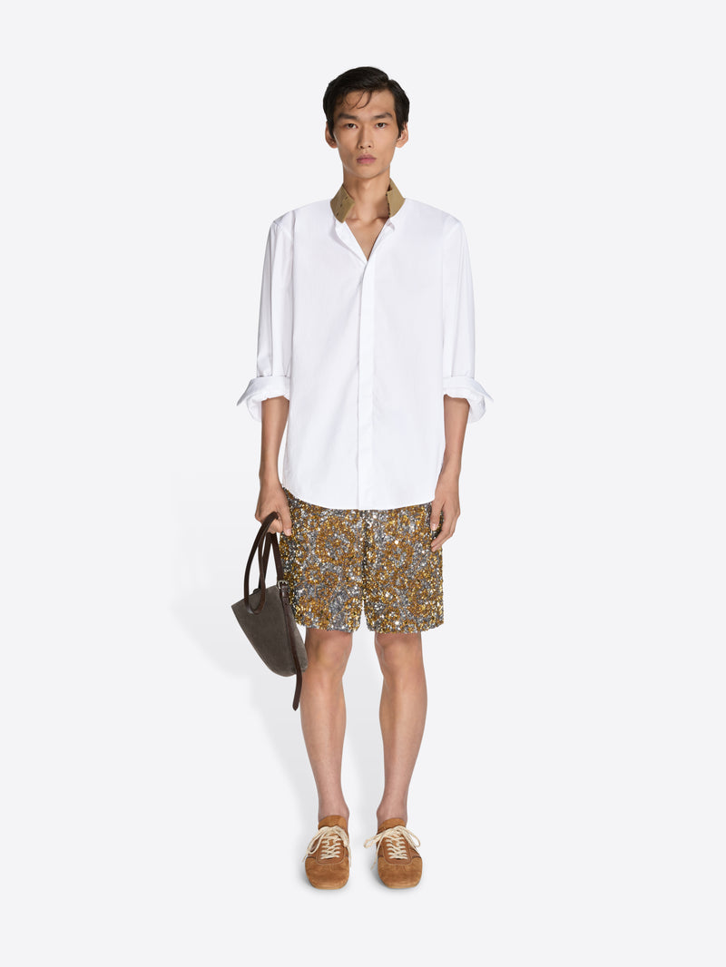 Person wearing a white shirt and patterned shorts on a white background